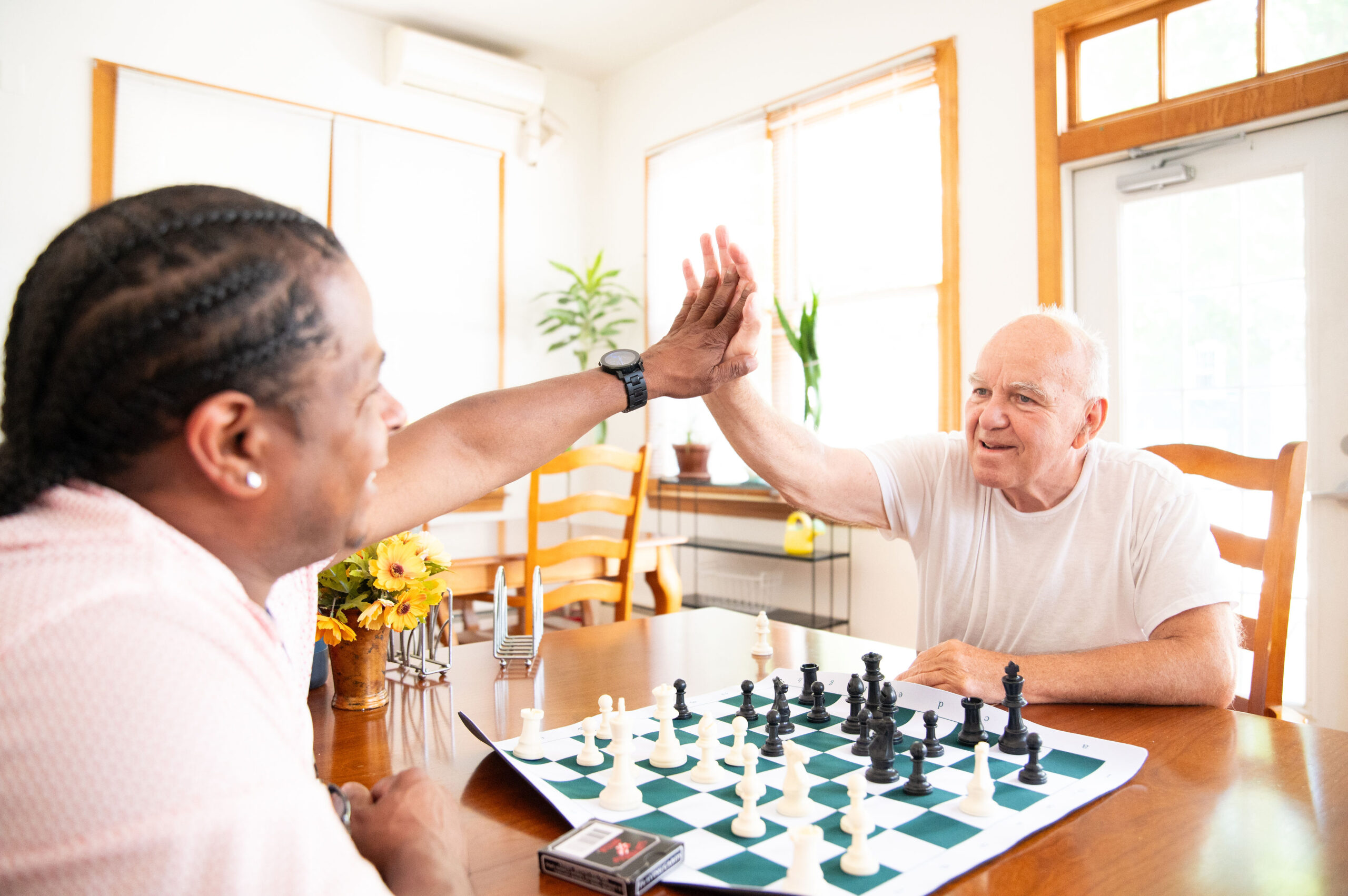 Two older adults playing chess and high fiving each other over the board.