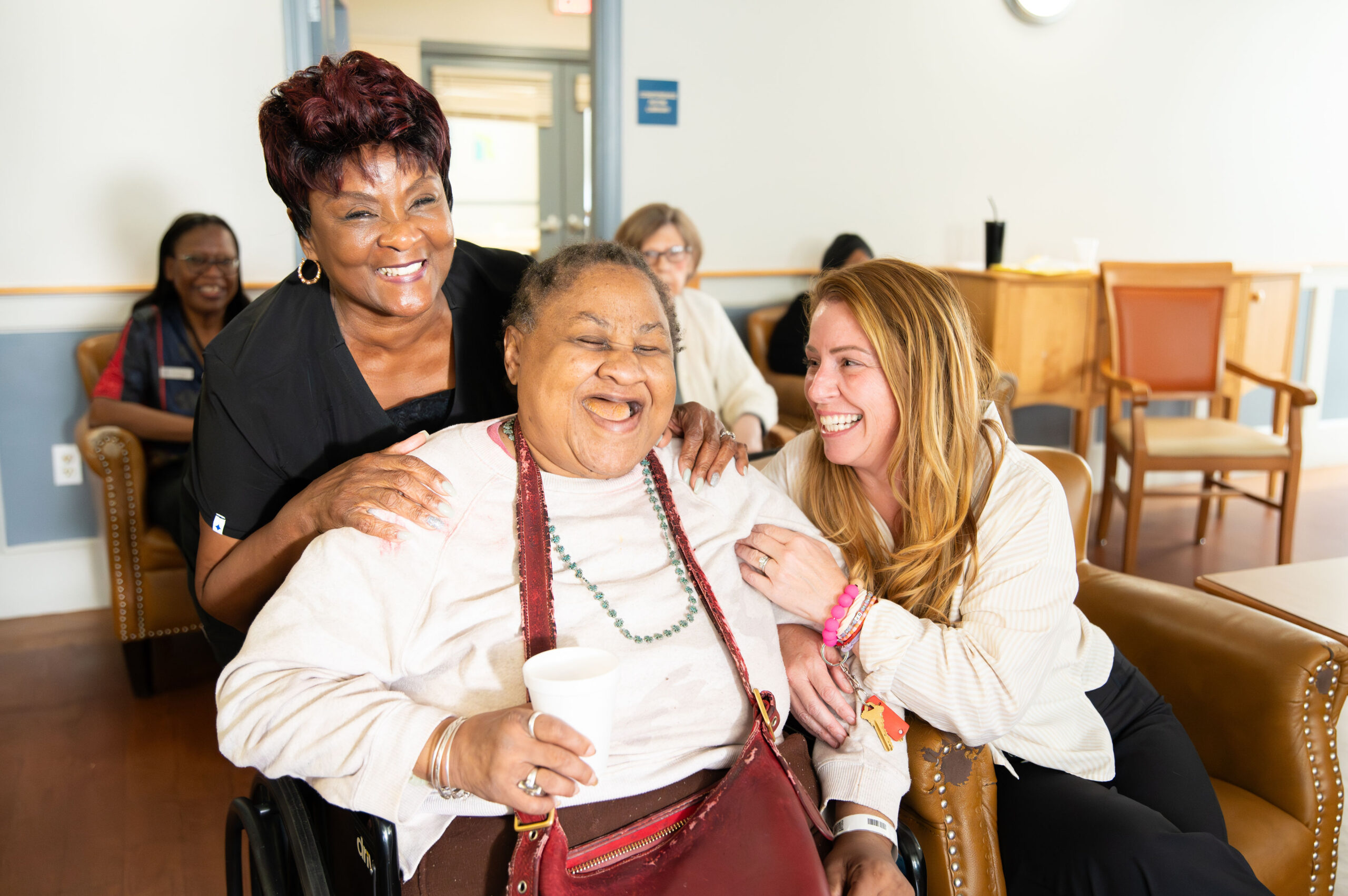 Three women laughing together in a warm, comfortable office setting.